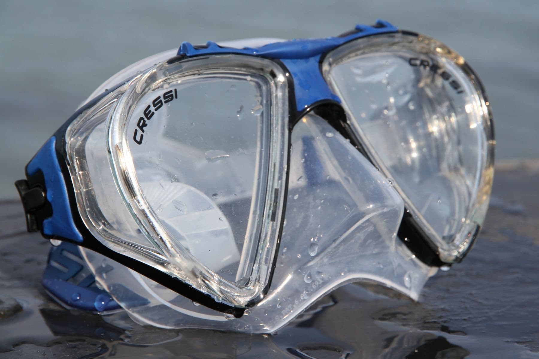 Close-up of the Cressi Penta+ mask resting in shallow water with droplets across its clear skirt